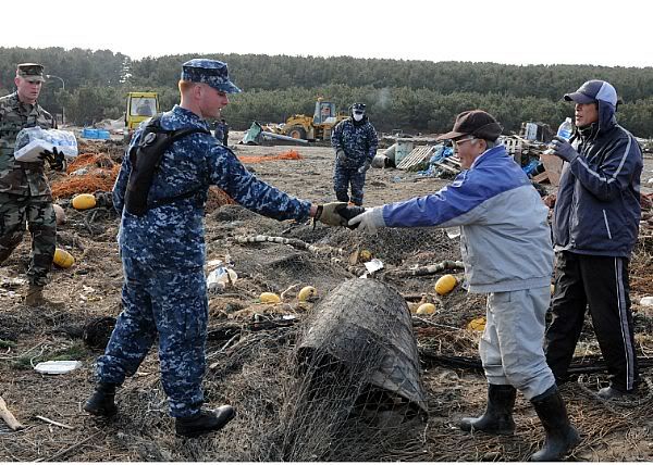 Mineman 2nd Class Cody Stone, from Phoenix, assigned to Naval Air Facility Misawa, recovers a spool of netting and returns it to a Japanese man during a volunteer cleanup at the Misawa Fishing Port.